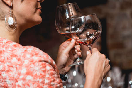 woman holds glass of wine. people consider the color of the wine and try how it smells in different...