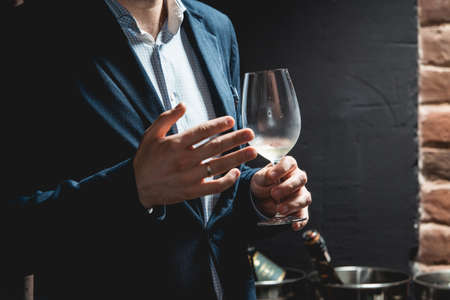 man holds glass of wine. people consider the color of the wine and try how it smells in different...