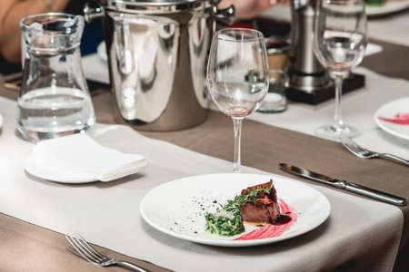 fresh grilled bbq roast beef steak and sauce on a white plate with green leaf of salad. soup sauce small jug glass served on a table in a restaurantの写真素材
