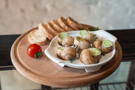Snails with herbs butter, in traditional ceramic pan bread on a wooden plank. Glass of wineの写真素材