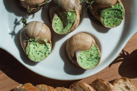 Snails with herbs butter, in traditional ceramic pan bread on a wooden plank.の写真素材