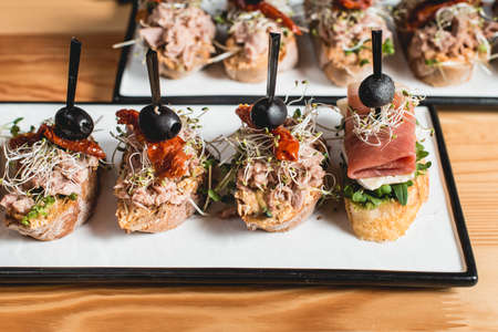 tasty pinchos with tuna, dried tomatoes, olive and pesto sauce, traditional spanish snack, served on a white plateの写真素材