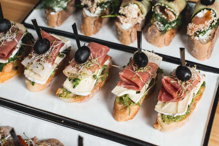 tasty pinchos with Hamon, Brie Cheese, Olives and Pesto Sauce, traditional spanish snack, served on...
