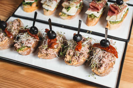 tasty pinchos with tuna, dried tomatoes, olive and pesto sauce, traditional spanish snack, served on a white plateの写真素材