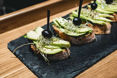 tasty pinchos with avocado, olive and basil pesto sauce, traditional spanish snack, served on a...
