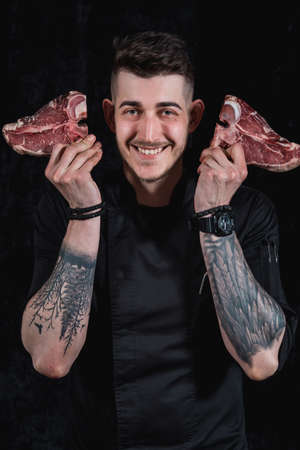 Smiling chef plays with raw meat steaks. Close-up in the kitchenの写真素材