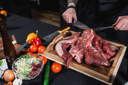 raw meat different kinds on a board on a table. Knife and fork in hands of the chef. Cook offers...