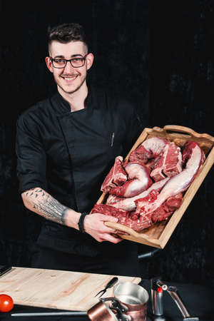 raw meat different kinds . Meat board in the hands of the smiling chef offers steaks to choose from. Close-up in the kitchenの写真素材