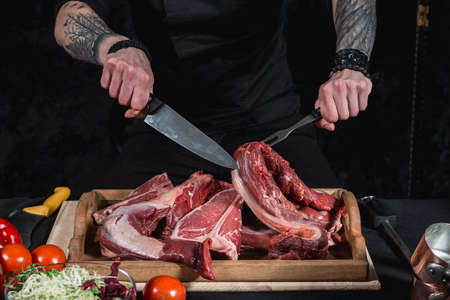 raw meat different kinds on a board on a table. Knife and fork in hands of the chef. Cook offers steaks to choose from. Close-up in the kitchenの写真素材