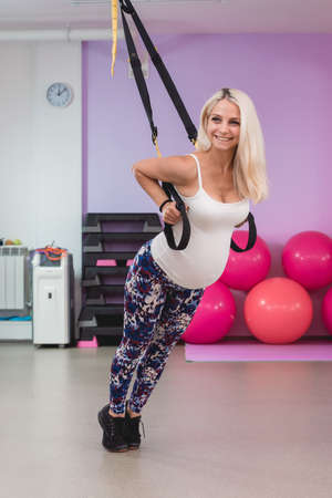 Young pregnant attractive woman training with trx fitness straps in the gyms studioの写真素材