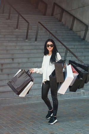 Beautiful girl in sunglasses with paper bags walking out of shopping mallの写真素材