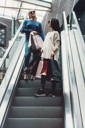 Beautiful girls with paper bags on escalator at supermarket