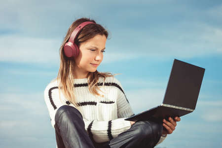 11 years girl in a wireless headphones listening to a music from a smart phone on a beach. against a blue sky. close upの写真素材