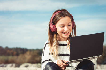 11 years girl in a wireless headphones listening to a music from a smart phone on a beach. against a blue sky. close upの写真素材