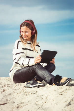 11 years girl in a wireless headphones listening to a music from a smart phone on a beach. against a blue sky. close upの写真素材
