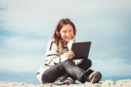 11 years girl in a wireless headphones listening to a music from a smart phone on a beach. against a blue sky. close upの写真素材