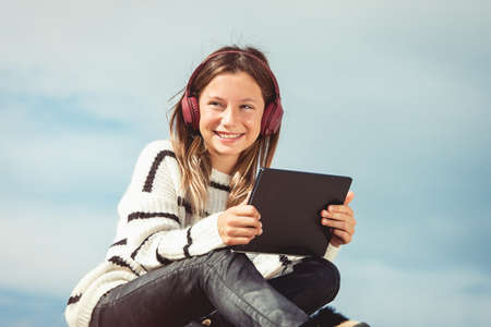 11 years girl in a wireless headphones listening to a music from a smart phone on a beach. against a blue sky. close upの写真素材