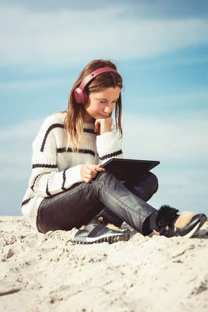 11 years girl in a wireless headphones listening to a music from a smart phone on a beach. against a blue sky. close upの写真素材