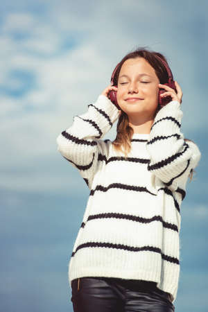 11 years girl in a wireless headphones listening to a music from a smart phone on a beach. against a blue sky. close upの写真素材
