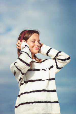 11 years girl in a wireless headphones listening to a music from a smart phone on a beach. against a blue sky. close upの写真素材