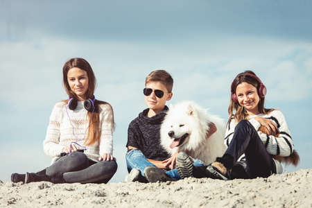 Happy 11 year old boy hugging his dog breed Samoyed at the seashore against a blue sky close up. Best friends rest and have fun on vacation, play in the sandの写真素材