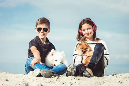 Happy 11 year old boy hugging his dog breed Samoyed at the seashore against a blue sky close up. Best friends rest and have fun on vacation, play in the sandの写真素材
