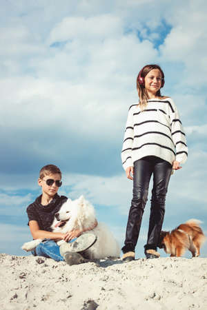 Happy 11 year old boy hugging his dog breed Samoyed at the seashore against a blue sky close up. Best friends rest and have fun on vacation, play in the sandの写真素材