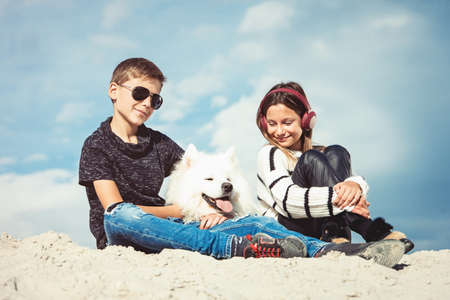 Happy 11 year old boy hugging his dog breed Samoyed at the seashore against a blue sky close up. Best friends rest and have fun on vacation, play in the sandの写真素材