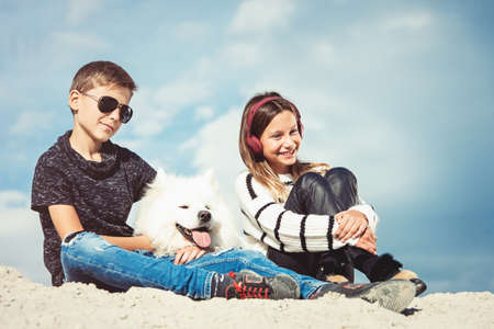 Happy 11 year old boy hugging his dog breed Samoyed at the seashore against a blue sky close up. Best friends rest and have fun on vacation, play in the sandの写真素材