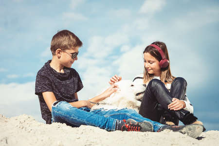 Happy 11 year old boy hugging his dog breed Samoyed at the seashore against a blue sky close up. Best friends rest and have fun on vacation, play in the sandの写真素材