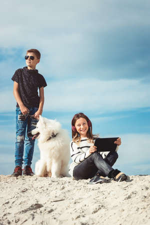 Happy 11 year old boy withhis dog breed Samoyed at the seashore against a blue sky close up. Best friends rest and have fun on vacation, play in the sandの写真素材