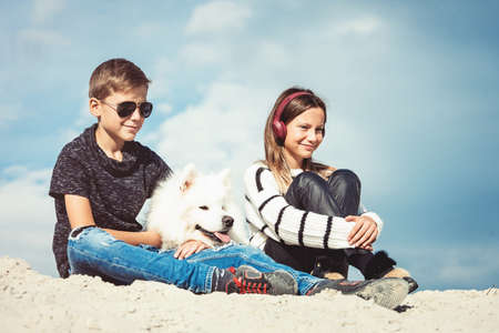 Happy 11 year old boy hugging his dog breed Samoyed at the seashore against a blue sky close up. Best friends rest and have fun on vacation, play in the sandの写真素材