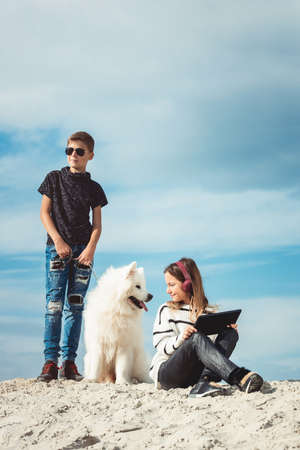 Happy 11 year old boy withhis dog breed Samoyed at the seashore against a blue sky close up. Best friends rest and have fun on vacation, play in the sandの写真素材