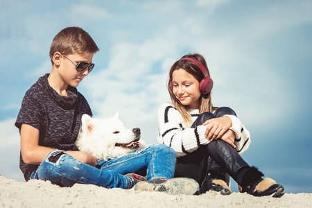 Happy 11 year old boy hugging his dog breed Samoyed at the seashore against a blue sky close up. Best friends rest and have fun on vacation, play in the sandの写真素材