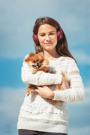 14 years girl in a wireless headphones listening to a music from a smart phone on a beach. against a blue sky. close upの写真素材
