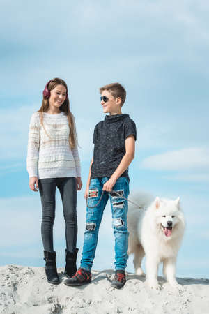 Happy 11 year old boy withhis dog breed Samoyed at the seashore against a blue sky close up. Best friends rest and have fun on vacation, play in the sandの写真素材