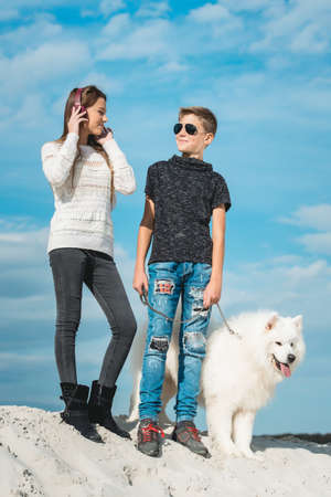 Happy 11 year old boy withhis dog breed Samoyed at the seashore against a blue sky close up. Best friends rest and have fun on vacation, play in the sandの写真素材