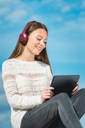 14 years girl in a wireless headphones listening to a music from a smart phone on a beach. against a blue sky. close upの写真素材
