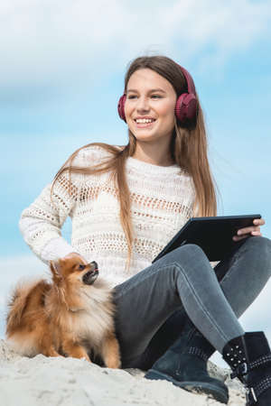 14 years girl in a wireless headphones listening to a music from a smart phone on a beach. against a blue sky. close upの写真素材