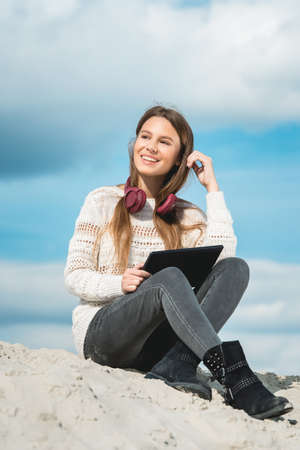 12 years girl in a wireless headphones listening to a music from a smart phone on a beach. against a blue sky. close upの写真素材