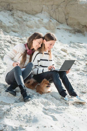 14 years girl with a wireless headphones sitting on a beach. close up. another girl have a notebook in her handsの写真素材