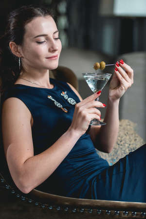 Fashionable gorgeous girl in a dark blue dress drinking cocktail in a luxery hotel lobby bar