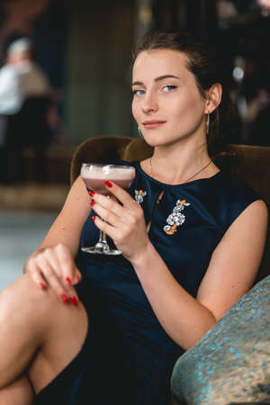 Fashionable gorgeous girl in a dark blue dress drinking cocktail in a luxery hotel lobby barの写真素材