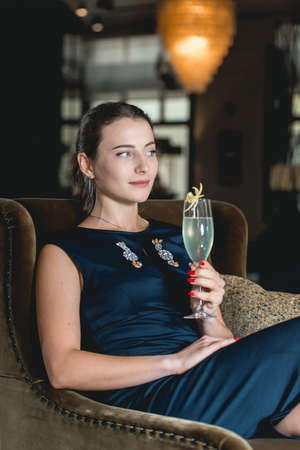 Fashionable gorgeous girl in a dark blue dress drinking cocktail in a luxery hotel lobby barの写真素材