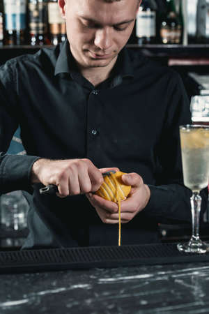 bartender making cocktail. slicing a long ribbon of lemon peel