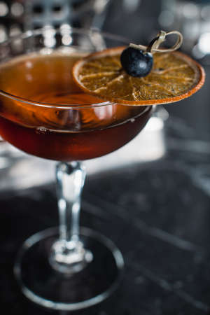 The Boulevardier Cocktail with orange chips on top. On a bar desk