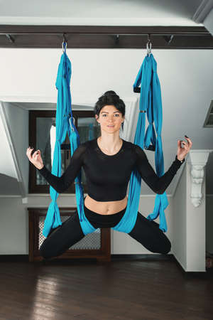 Yoga in a white room. woman performs physical exercises fly-yoga, pilates on a special equipmentの写真素材
