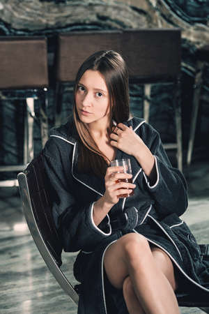 Portrait of young beautiful woman relaxing in a chair in a bathrobe with a detox drink in a hand. Luxery spa centerの写真素材
