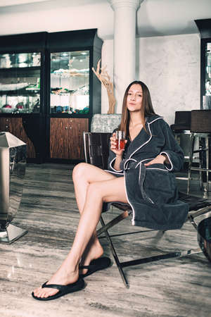 Portrait of young beautiful woman relaxing in a chair in a bathrobe with a detox drink in a hand. Luxery spa centerの写真素材