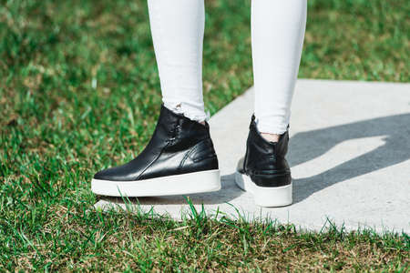 Rear View Of Woman's Black Leather Ankle Boots. Outdoor Shot Over White Stone in park. white soleの写真素材